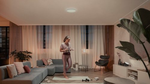Person exercising in a modern living room, illuminated by a round ceiling light and accent lighting, with fitness equipment nearby.