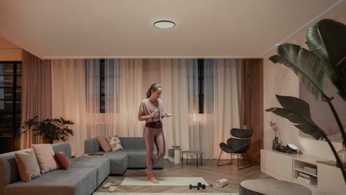 Person exercising on a yoga mat in a modern living room, supported by overhead ceiling light and soft ambient lighting.