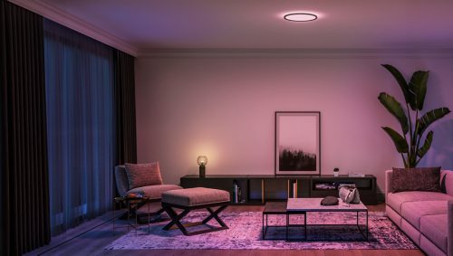 Modern living room with a round slim ceiling light emitting a soft ambient glow, highlighting neutral furniture and decor.