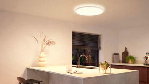 Round slim ceiling light fixture mounted above a kitchen island, emitting bright white light onto the countertop below.