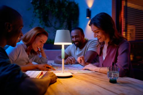 Group of people gathered outdoors around a table, planning with a map illuminated by a portable table lamp.