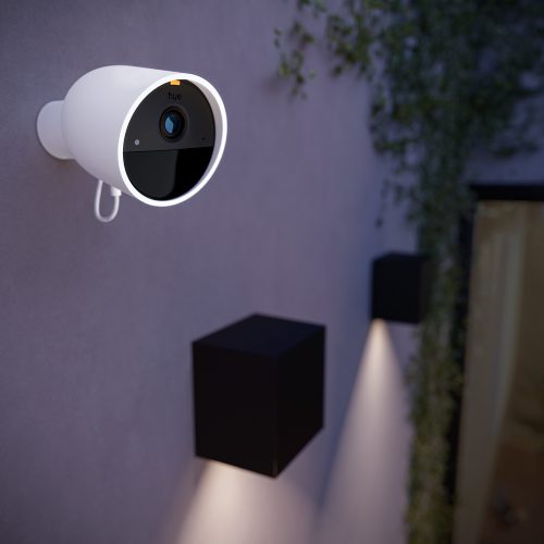 A white outdoor security camera with a circular LED ring is wall-mounted above cube-shaped wall lights, facing outward.