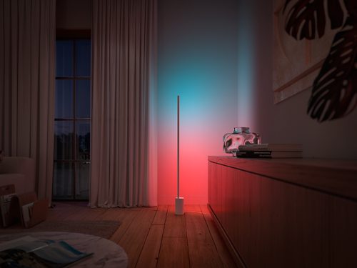 Vertical floor lamp positioned beside a cabinet, casting gradient red and blue light onto the wall and nearby surfaces.