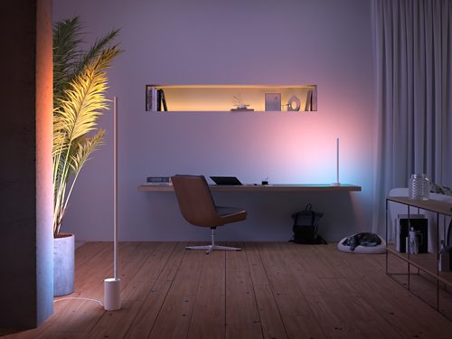 Vertical smart light bars placed on the floor and desk, emitting gradient light onto nearby wall and plant, enhancing workspace visibility.