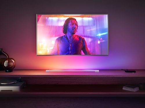 Light tube placed on shelf below a television, projecting gradient colored light onto the wall and surrounding surfaces.