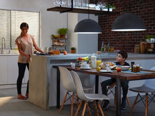 A group of people enjoying breakfast in a modern kitchen, with pendant lights illuminating the dining table and food.