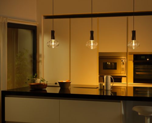 Pendant smart bulbs with clear glass design are suspended above a kitchen island, casting focused light onto the countertop.